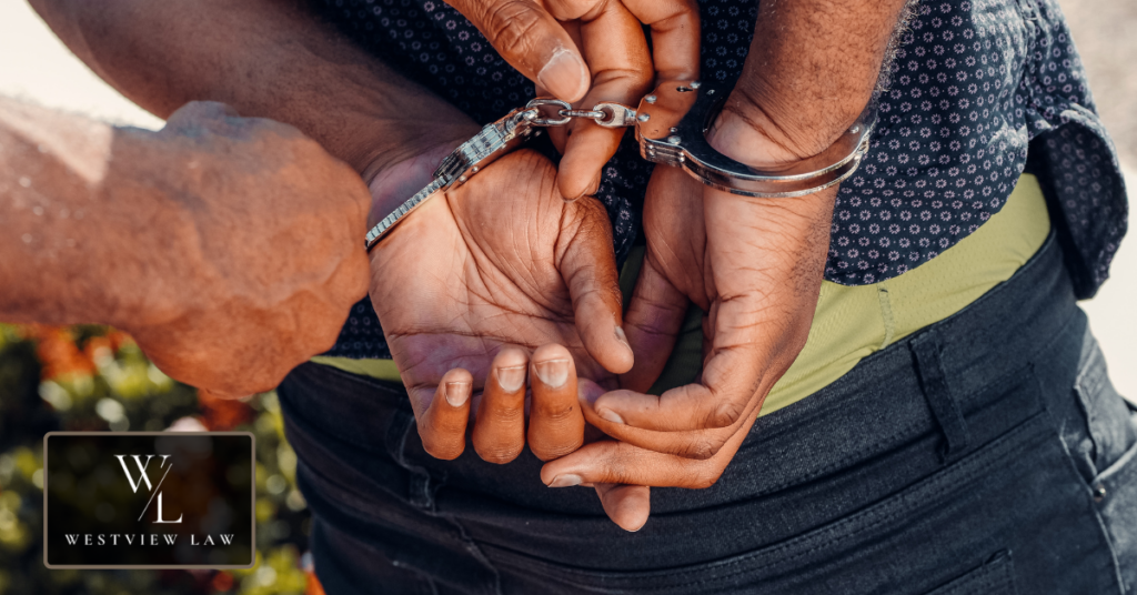 Close-up of a worker's hands being cuffed behind their back, illustrating the criminal charges an employer can face for wage theft in California