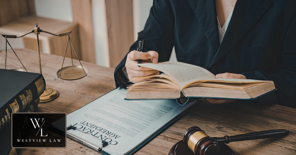 Attorney at a desk reading a law book beside a contract agreement, scales of justice and a gavel